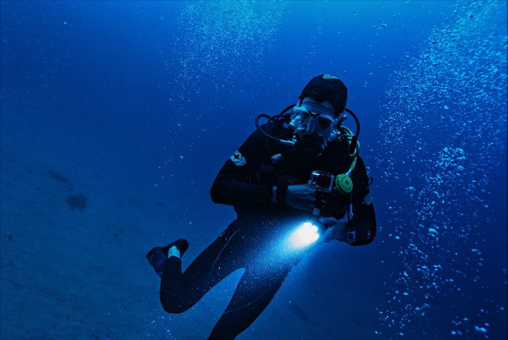 pexels-photo-3098970 A scuba diver exploring the deep ocean with a flashlight, surrounded by bubbles and marine life.